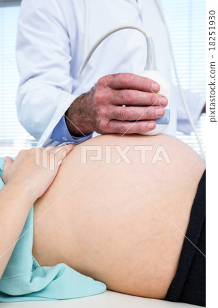 Midsection of doctor performing ultrasound on woman 18251930