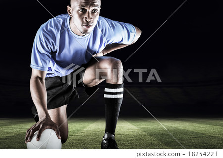 Composite image of serious rugby player kneeling while holding b Composite image of serious rugby player kneeling while holding b 18254221