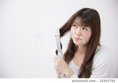 A woman who arranges her hair with a hair iron 18303798