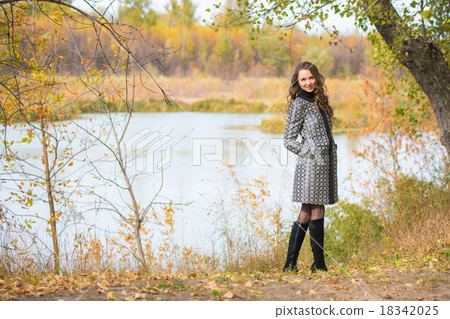 A young girl walks by the river in the autumn forest 18342025