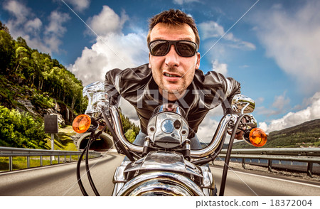 Funny Biker in sunglasses and leather jacket racing on mountain Funny Biker in sunglasses and leather jacket racing on mountain 18372004