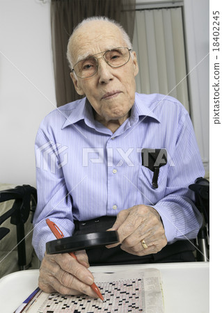 elderly man sitting doing crosswords hobby 18402245