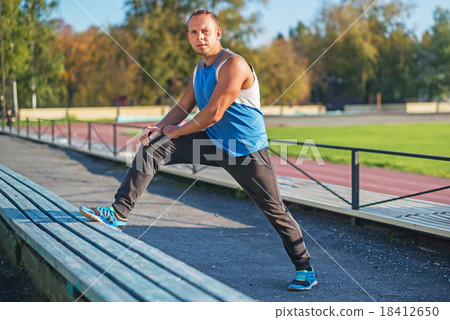 man trains, stretched on bench  stadium.  18412650