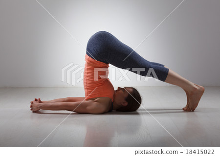 Sporty woman practices yoga asana Halasana 18415022