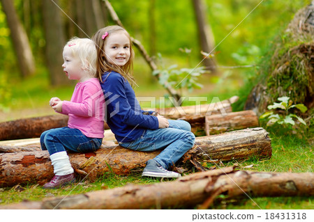 Two little sisters sitting on a log in a forest 18431318