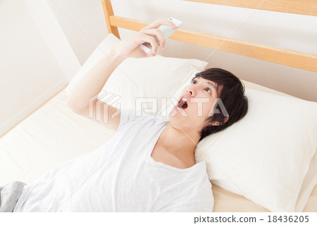 一個驚訝的醒來的人看著智能手機 18436205