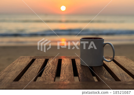 Coffee cup on wood table at sunset or sunrise beach 18521087