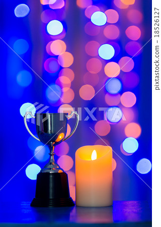 Silver cup trophy and candle against blue bokeh Silver cup trophy and candle against blue bokeh 18526127