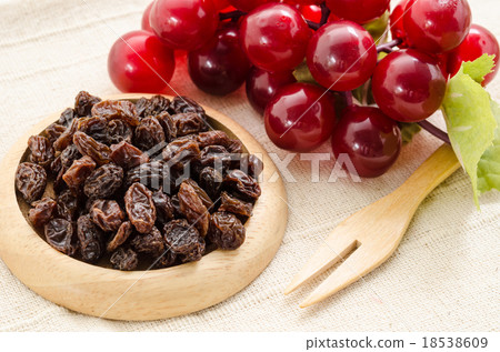 Raisins on a wooden dish and fresh red grapes. 18538609
