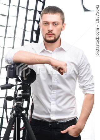 Young attractive photographer leaning on tripod Young attractive photographer leaning on tripod 18575042