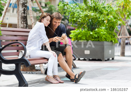 Mix race couple using cell smart phone sitting in 18610287