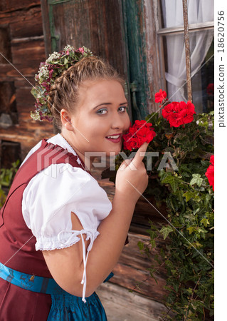 Bavarian girl in dirndl smelling a geranium. 18620756