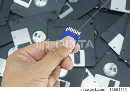 Hand holding SD card with floppy disk background 18661513