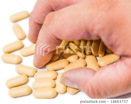 Male's hand grabs yellow vitamin  tablets isolated 18663737