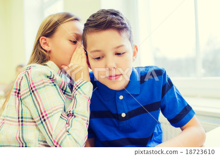 smiling schoolgirl whispering to classmate ear 18723610