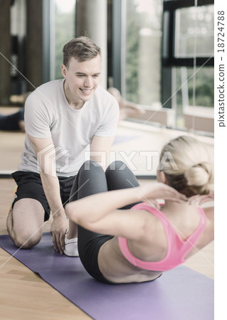 smiling woman with male trainer exercising in gym 18724788