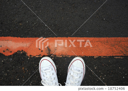 White sneaker shoes standing behind the red line. 18752406
