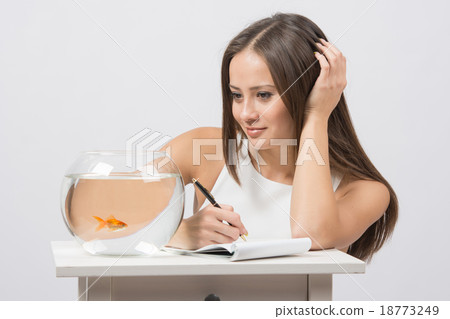 Girl writing in a notebook and looking at goldfish Girl writing in a notebook and looking at goldfish 18773249
