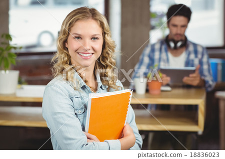 Portrait of smiling woman holding spiral notebook in office 18836023