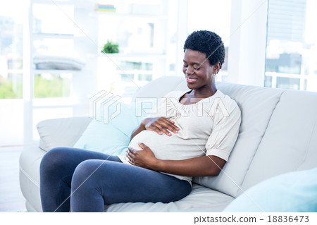 Pregnant woman touching her belly while sitting at home Pregnant woman touching her belly while sitting at home 18836473