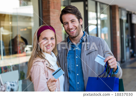 Smiling couple with shopping bags showing credit card Smiling couple with shopping bags showing credit card 18837030