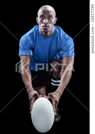 Portrait of rugby player holding ball while kneeling 18837299