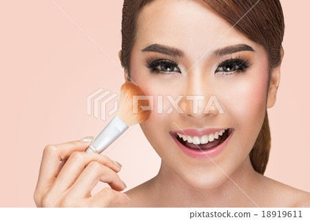 Portrait of young woman applying blusher 18919611