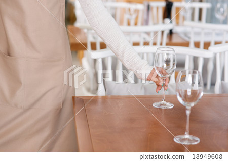 Waitress is putting water glasses on the tables. Waitress is putting water glasses on the tables. 18949608