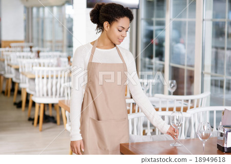 Waitress is putting water glasses on the tables. Waitress is putting water glasses on the tables. 18949618