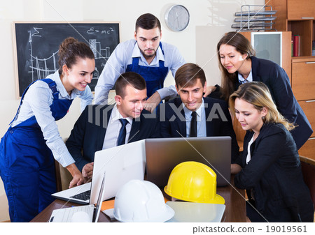 Engineers with laptops discussing project 19019561