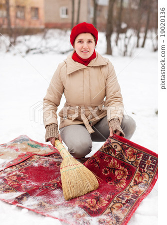 Stock Photo: woman in cap cleans carpet with snow