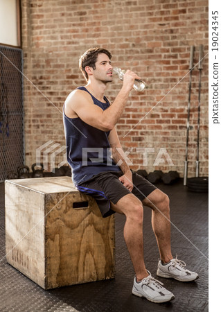 Man sitting on plyo box and drinking water Man sitting on plyo box and drinking water 19024345