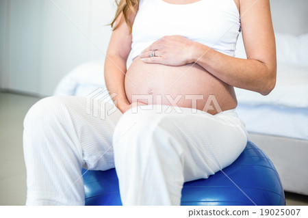 Midsection of pregnant woman sitting on ball 19025007