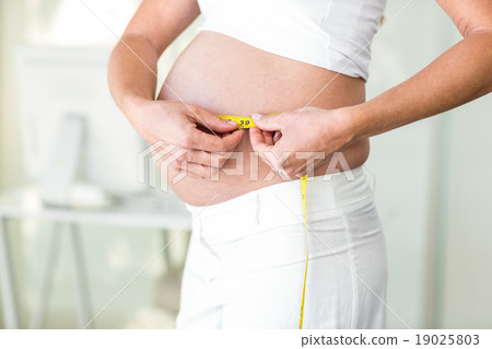 Midsection of woman measuring abdomen Midsection of woman measuring abdomen 19025803