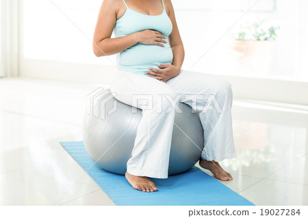 Pregnant woman sitting on exercise ball touching her belly Pregnant woman sitting on exercise ball touching her belly 19027284