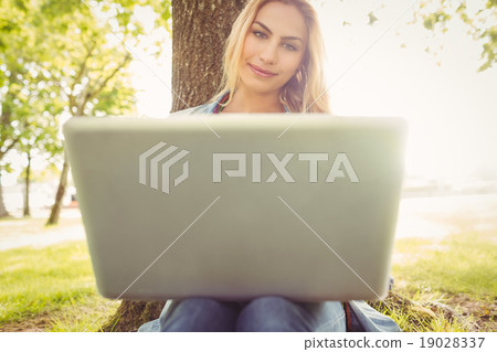 Smiling woman using laptop while sitting under tree Smiling woman using laptop while sitting under tree 19028337