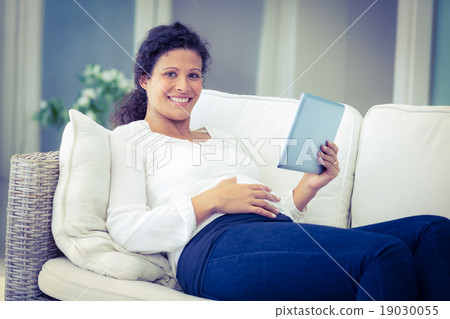 Portrait of happy woman reclining on sofa with tablet Portrait of happy woman reclining on sofa with tablet 19030055