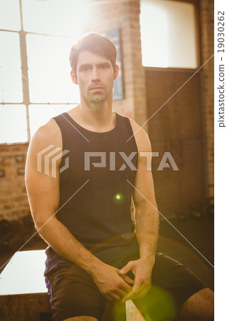 Muscular man sitting on plyo box 19030262