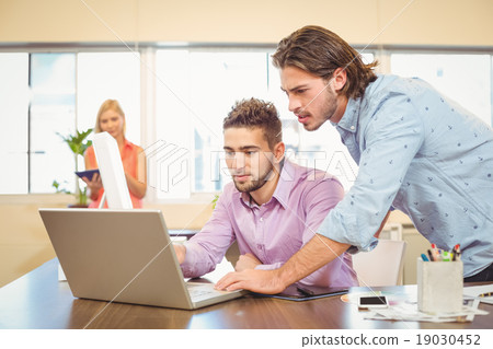 Businessmen working on laptop with female colleague in backgroun Businessmen working on laptop with female colleague in backgroun 19030452