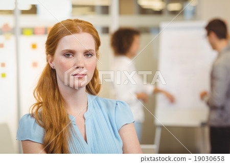 Serious businesswoman with arm crossed with colleagues in backgr Serious businesswoman with arm crossed with colleagues in backgr 19030658