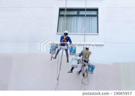Two worker are painting the color on high building 19065957