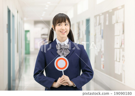 Posing school girls in uniform with standing ○ × sign at the school corridor 19090180