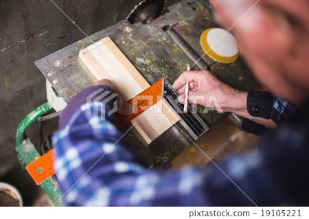 Old carpenter taking measurement of a wooden plank 19105221