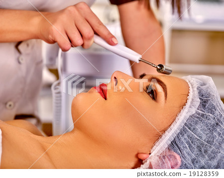 Young woman receiving electric facial massage. 19128359