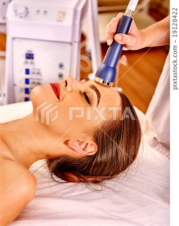 Young woman receiving electric facial massage. 19128422