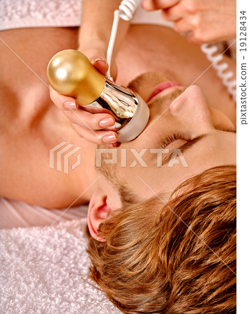 Young woman receiving electric facial massage. 19128434