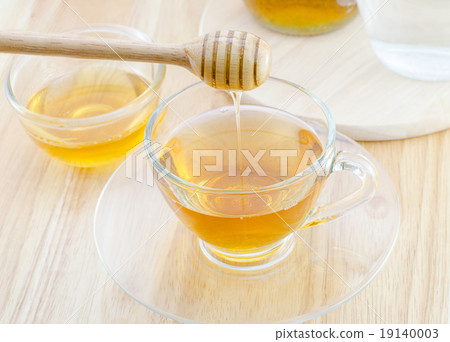 Pouring honey into cup of tea on wooden table Pouring honey into cup of tea on wooden table 19140003