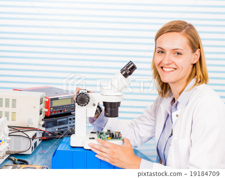 A young female researcher in a lab coat is peering into a micros 19184709