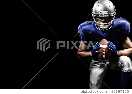 Composite image of determined american football player holding ball while kneeling 19197190