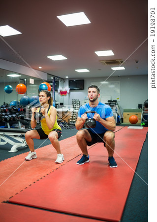 Couple crouching down while holding kettlebells 19198701